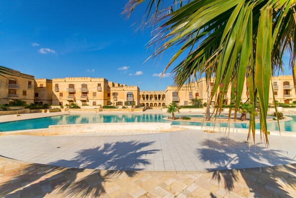 A pool area with a clear sky, palm trees, and buildings with balconies.