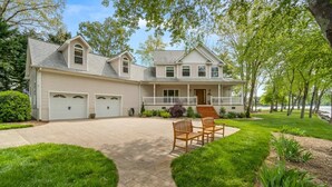 A two-story house with a covered driveway, a front porch, and a lawn with outdoor furniture.