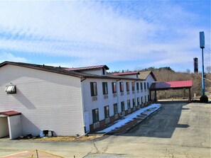 A row of white buildings with red roofs, a covered parking area, and a clear sky. - Marifah Inn (Williamsburg)
