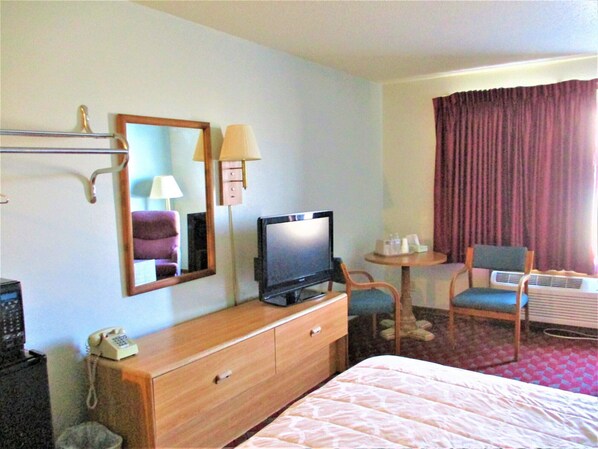 A hotel room with a bed, a television, a desk with a telephone, a chair, and a mirror. - Marifah Inn (Williamsburg)