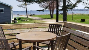 A wooden deck with a round table and chairs, overlooking a grassy area and a body of water. - #8 2bed 1bath LAKE MI Fishing Cabin WiFi AC Deck Firepit Kayak Paddle Boat Dock (Gladstone)