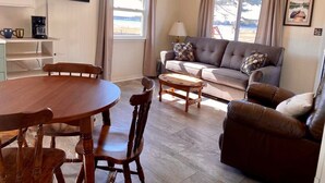 A cozy living room with a wooden dining table, a sofa, and a coffee table. - #8 2bed 1bath LAKE MI Fishing Cabin WiFi AC Deck Firepit Kayak Paddle Boat Dock (Gladstone)