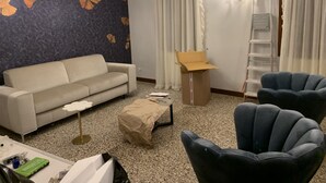 A living room with a sofa, two armchairs, a coffee table, a chandelier, a wall with a floral pattern, a ladder, and a partially open cardboard box. - San Marco Charming Suite apartment (Venezia)