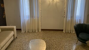 A living room with a beige sofa, a dark armchair, a white ottoman, and a chandelier. - San Marco Charming Suite apartment (Venezia)