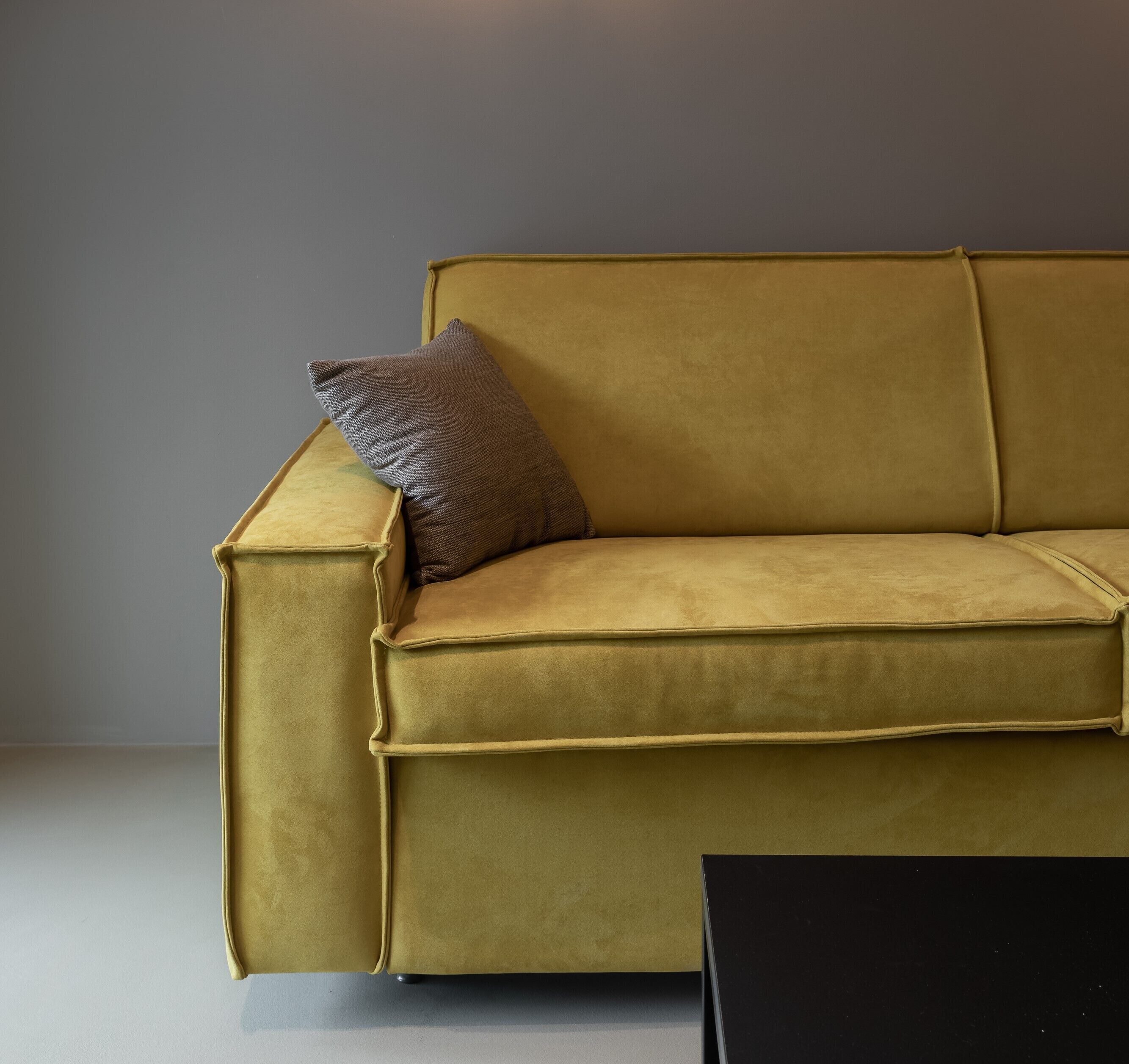 En sofa i sennepsfarve med en mørkebrun pude og et sort sofabord.