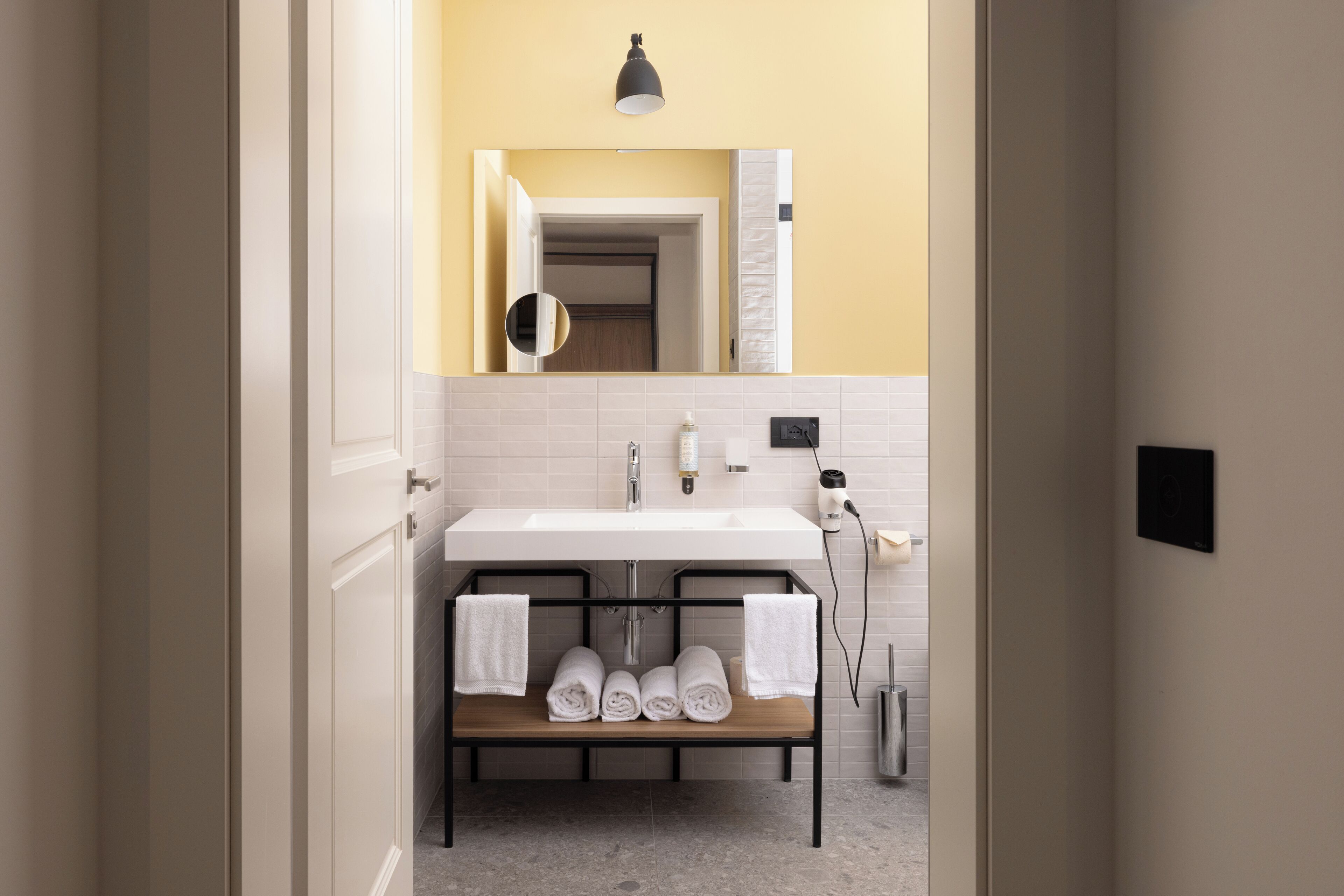 A modern bathroom with a white sink, a mirror above it, and a bench with towels.