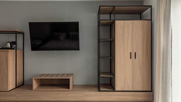 Quarto moderno com televisão de tela plana na parede, guarda-roupa de madeira com várias prateleiras e um pequeno banco de madeira.