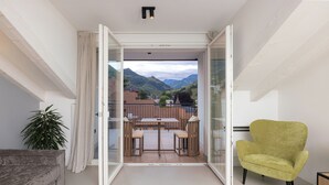 A balcony with a table and chairs, a green armchair, and a view of mountains. - Residence - Palais Hörtenberg (Bolzano)