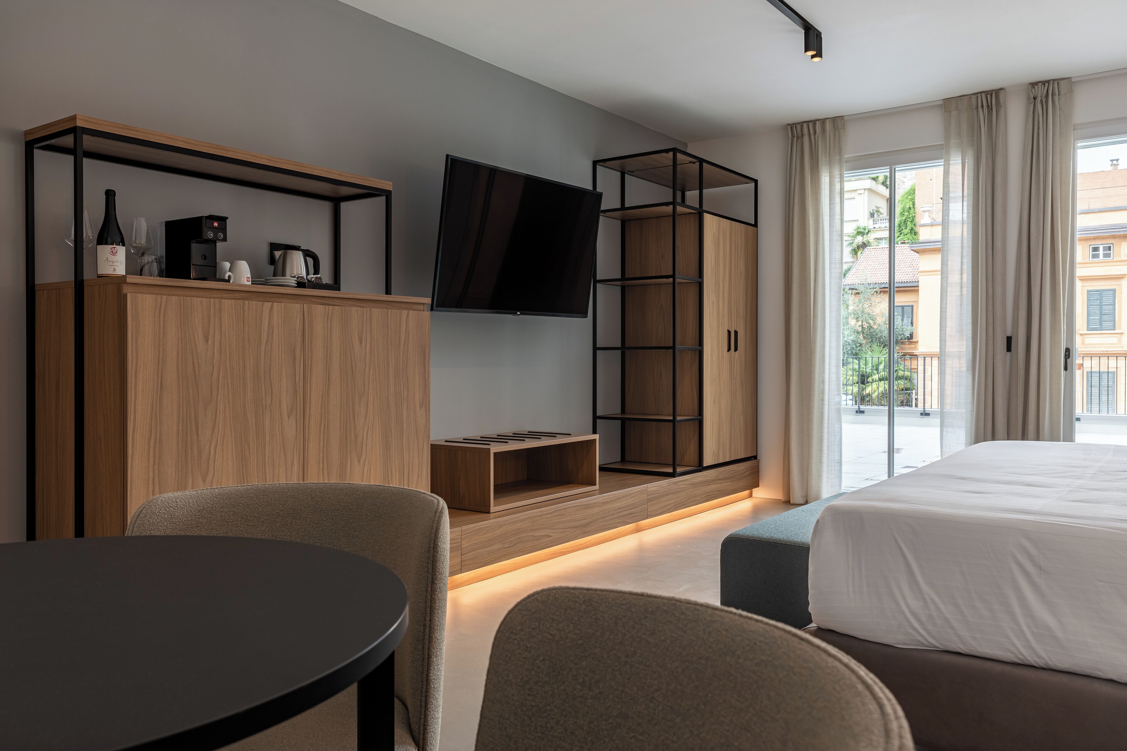 Ein modernes Hotelzimmer mit einem großen Bett, einem an der Wand montierten Fernseher, einem Holzschrank, einem kleinen Tisch und einer Sitzecke.