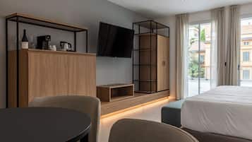Una camera d'albergo moderna con un letto grande, una TV fissata al muro, un armadio in legno, un tavolino e un angolo salotto.