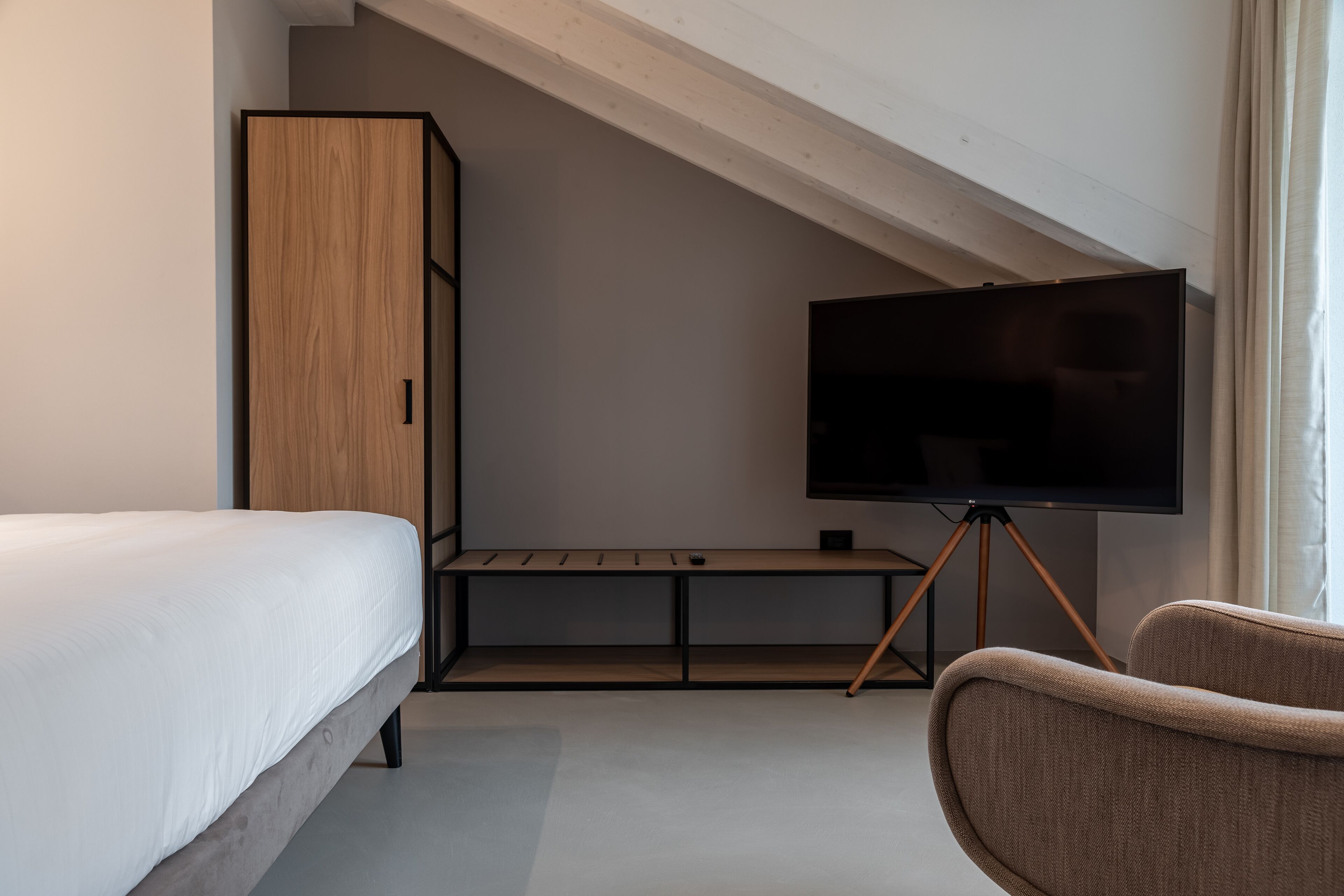 A bedroom with a bed, a TV on a stand, a wooden wardrobe, and a chair.