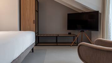A bedroom with a bed, a TV on a stand, a wooden wardrobe, and a chair.