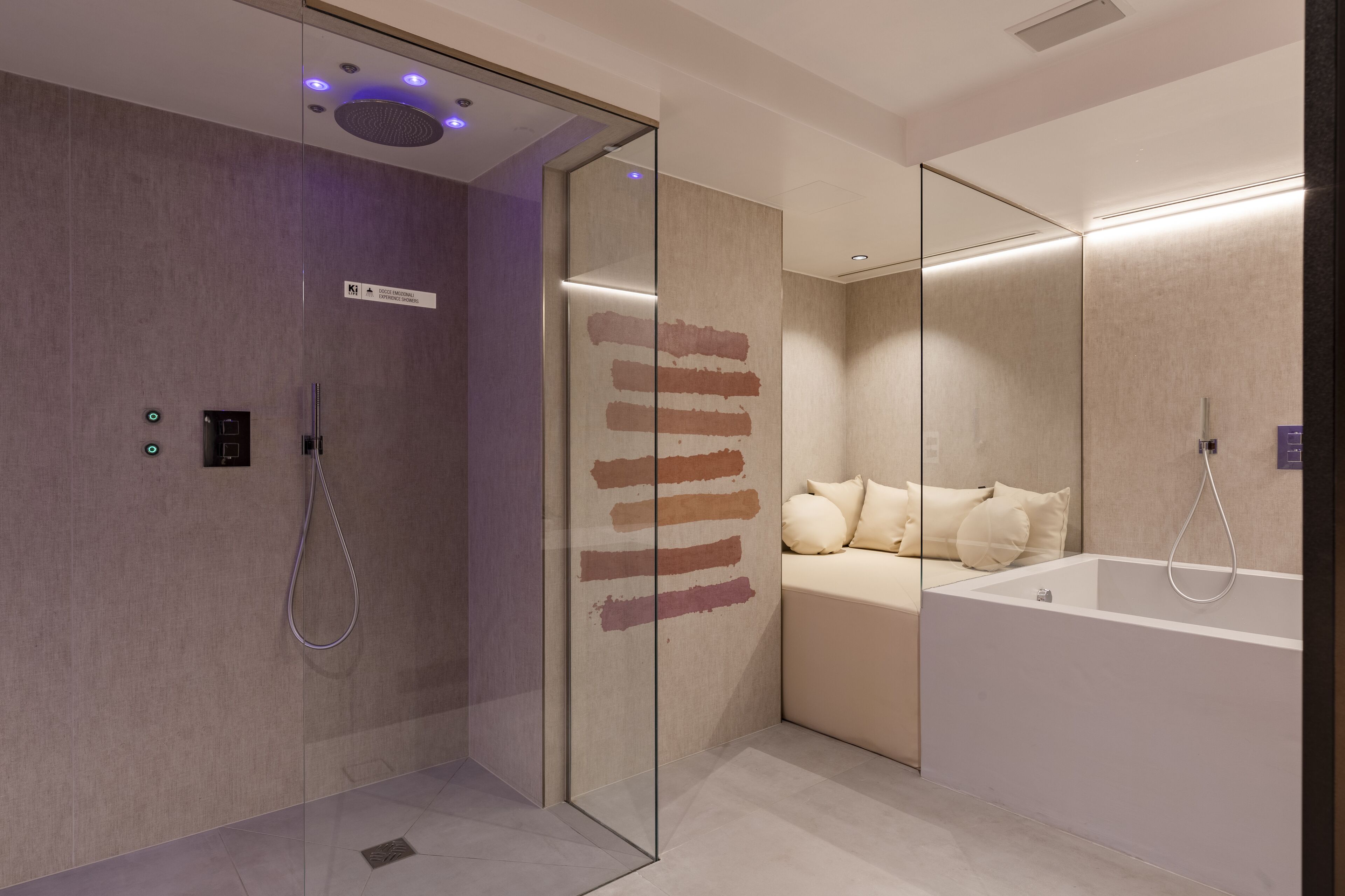 A modern bathroom with a glass shower enclosure, a large bathtub, and a seating area with a bench and pillows.