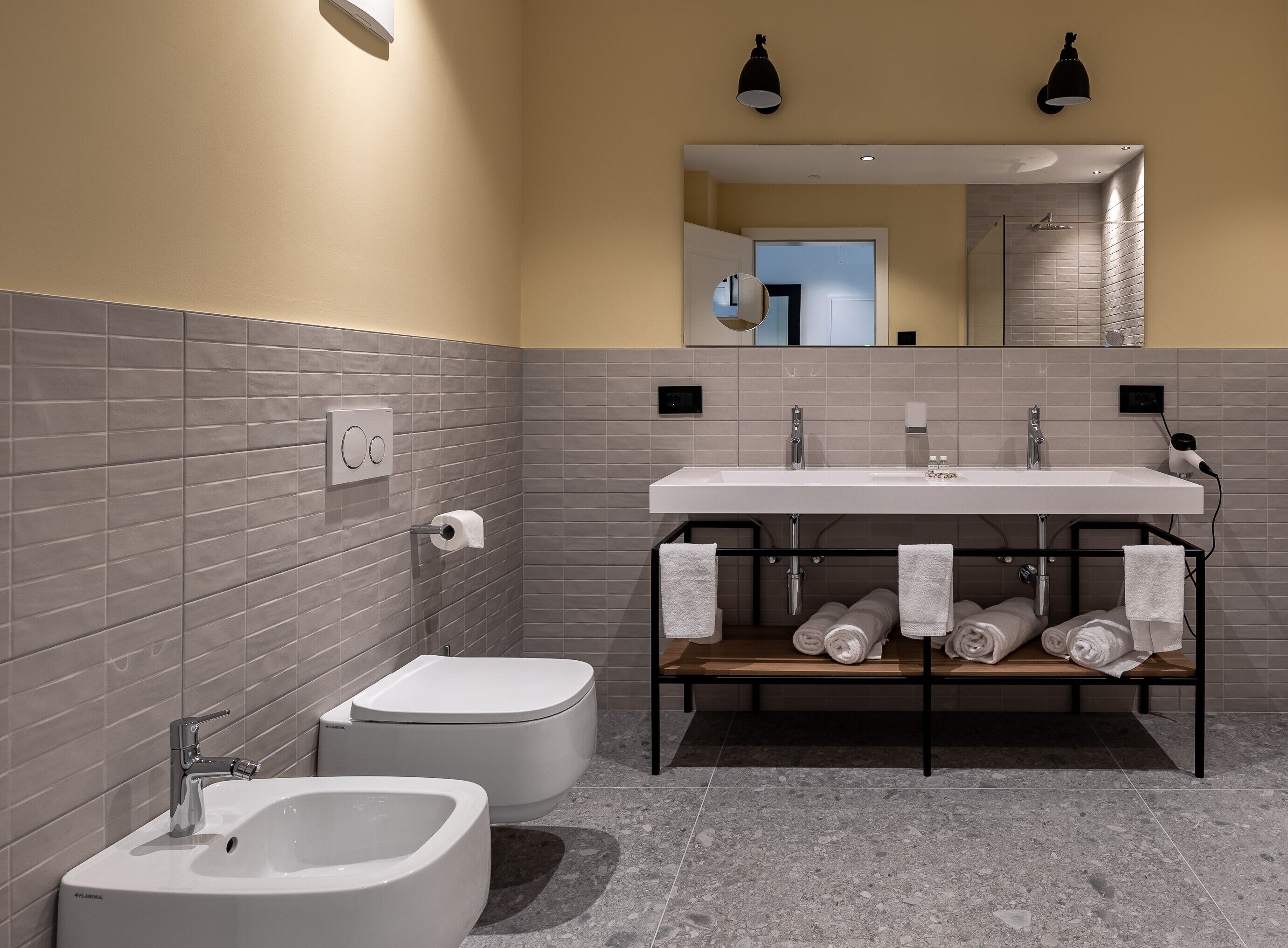 Un baño moderno con un lavamanos blanco, dos inodoros, un bidé y un perchero con toallas.