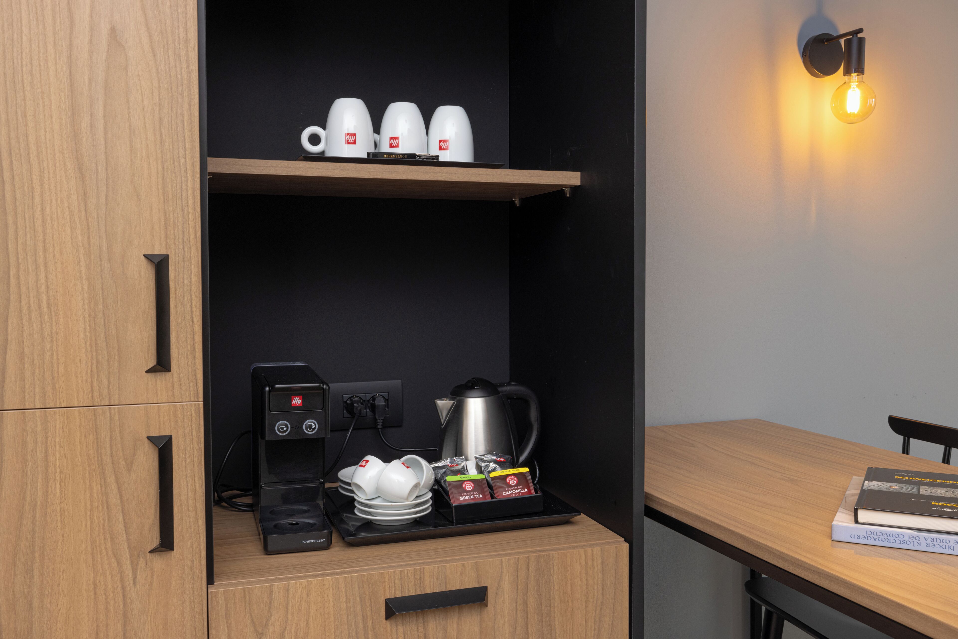 Una kitchenette compacta con cafetera, cápsulas de té y café, y tetera sobre una bandeja.