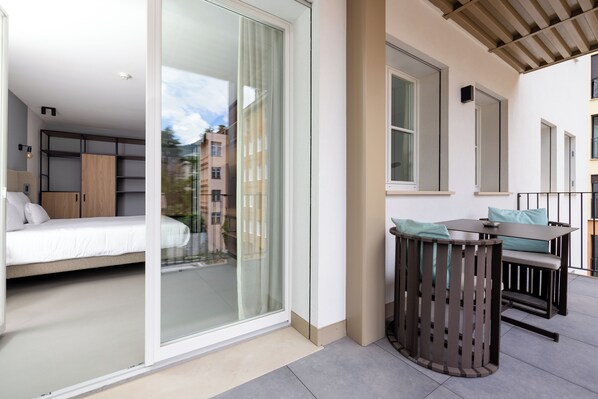 A modern apartment with a bed, a dining area, and a balcony with a view of neighboring buildings.