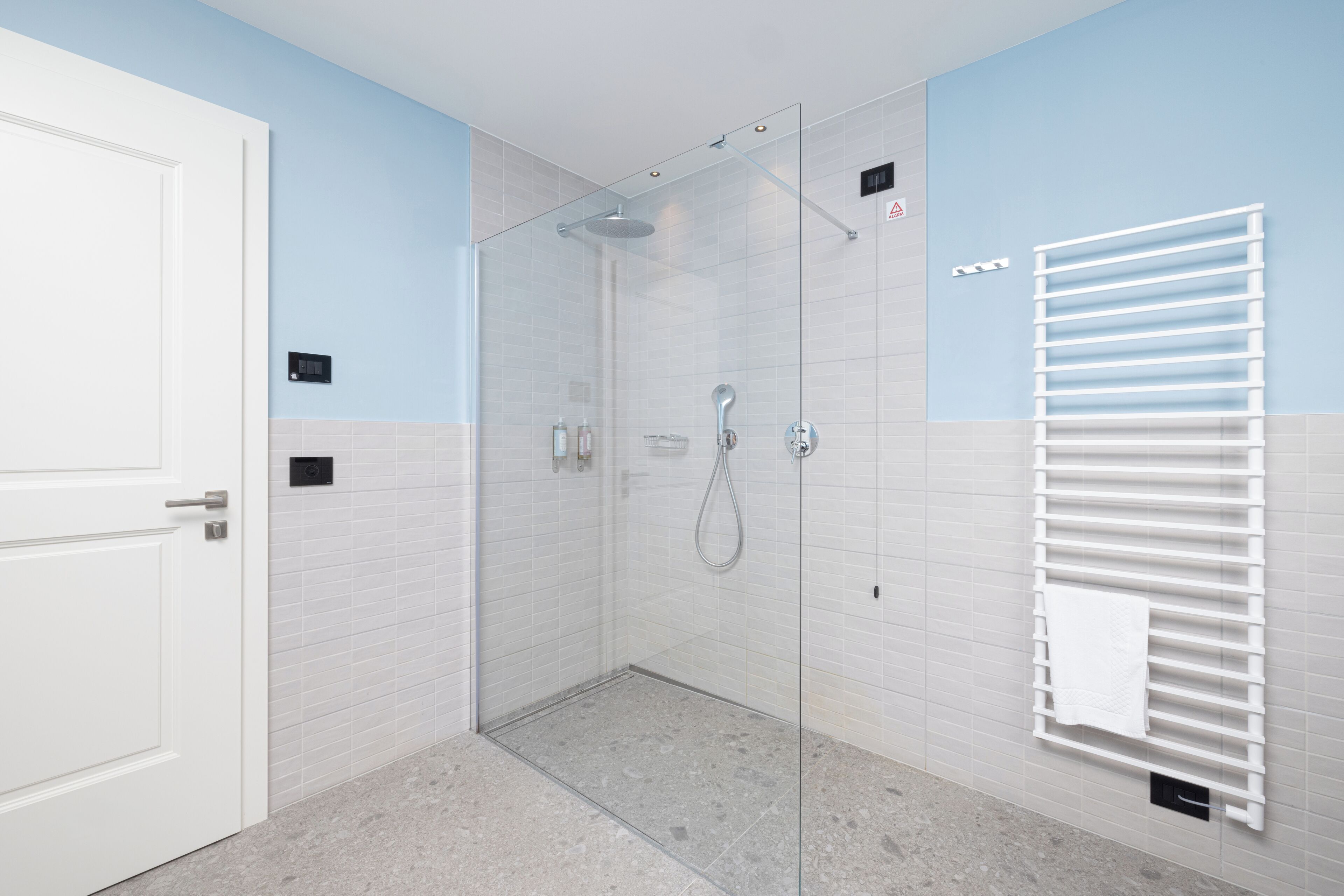 Une salle de bain moderne avec une douche à parois de verre, des murs recouverts de carreaux blancs et un porte-serviettes.