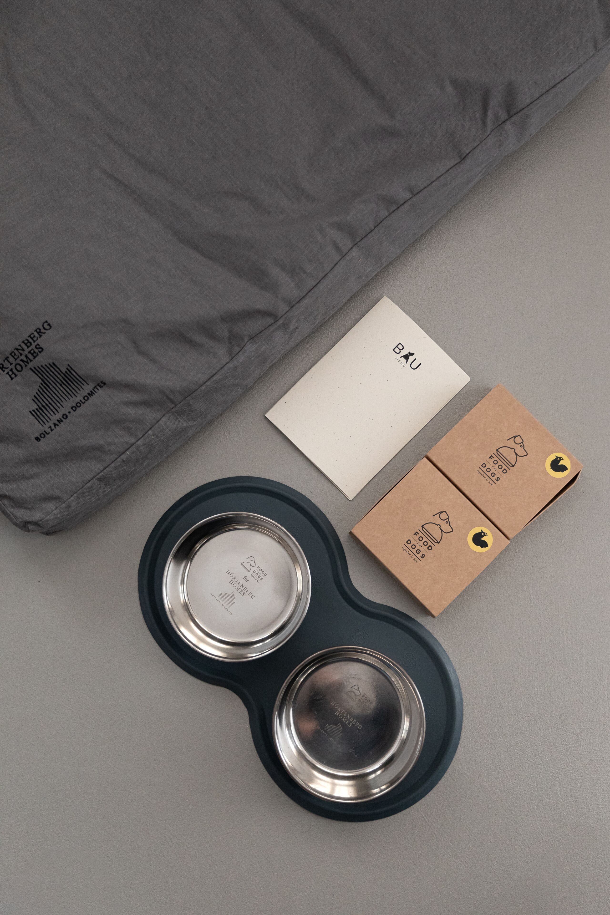 Una almohada gris, una tarjeta blanca y dos cajas de cartón con la marca de alimento para perros.