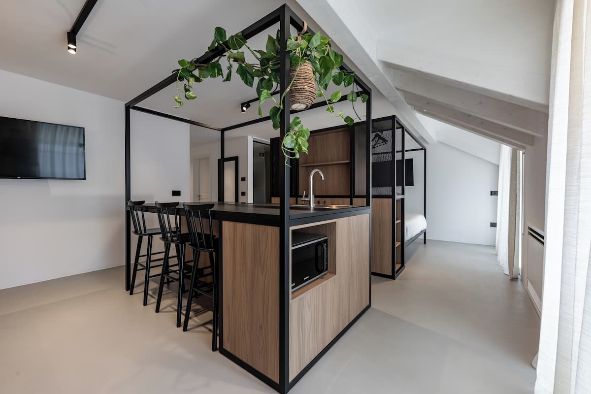 A modern kitchen with a central island, bar stools, a hanging plant, and a built-in microwave.