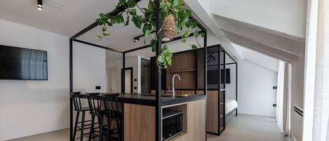 A modern kitchen with a central island, bar stools, a hanging plant, and a built-in microwave.