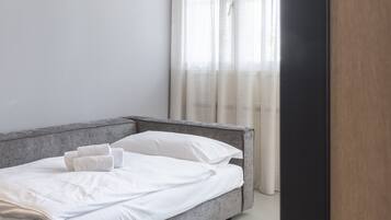 A modern bedroom with a grey bed, white linens, and sheer curtains.