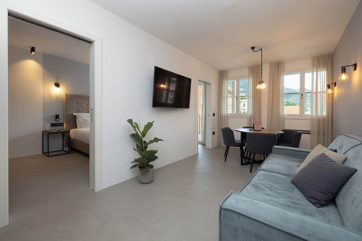 A modern living room with a sofa, a dining area, and a TV mounted on the wall.