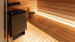 A sauna with wooden slats, a heater, and a small shelf with a container. - Residence - Palais Hörtenberg (Bolzano)