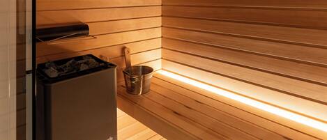 A sauna with wooden slats, a heater, and a small shelf with a container.
