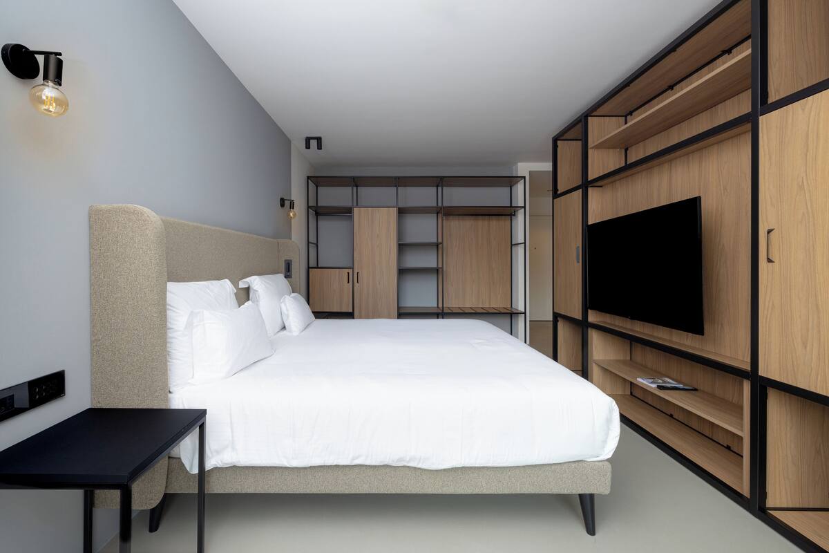A modern bedroom with a large bed, built-in wardrobe, and a flat-screen TV.