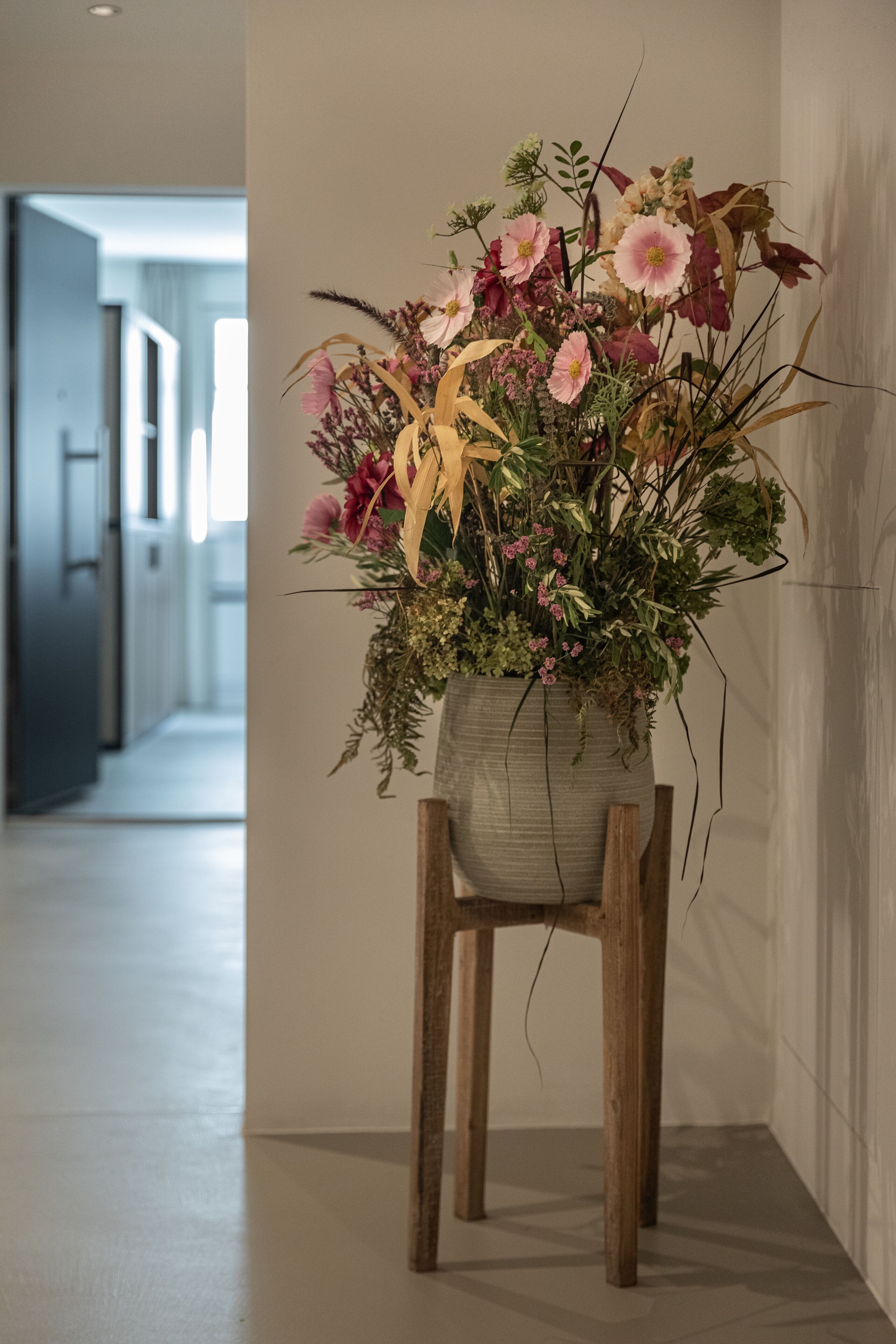 A floral arrangement in a vase on a wooden chair in a hallway.