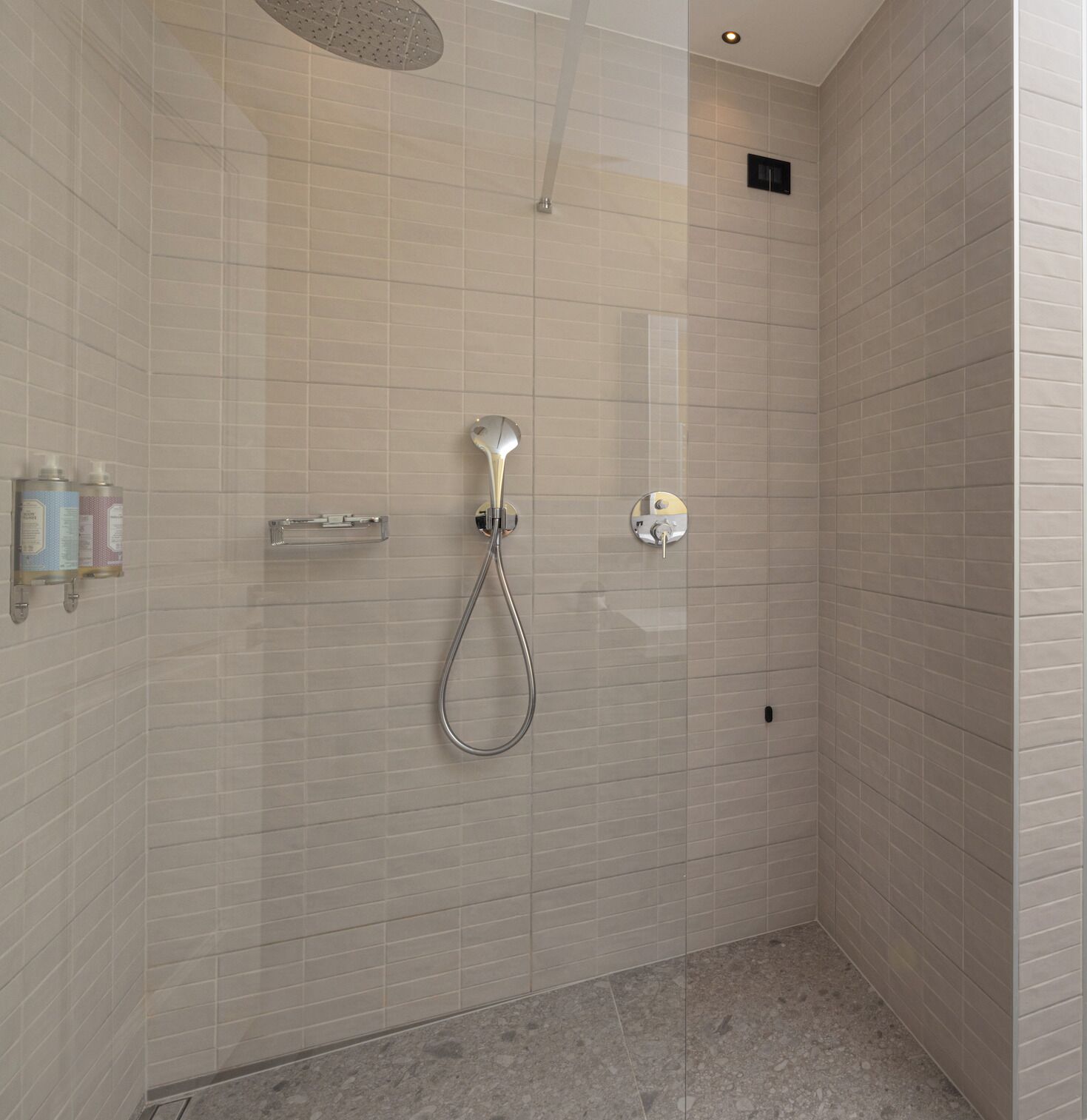 A modern shower with a handheld showerhead and a wall-mounted control.