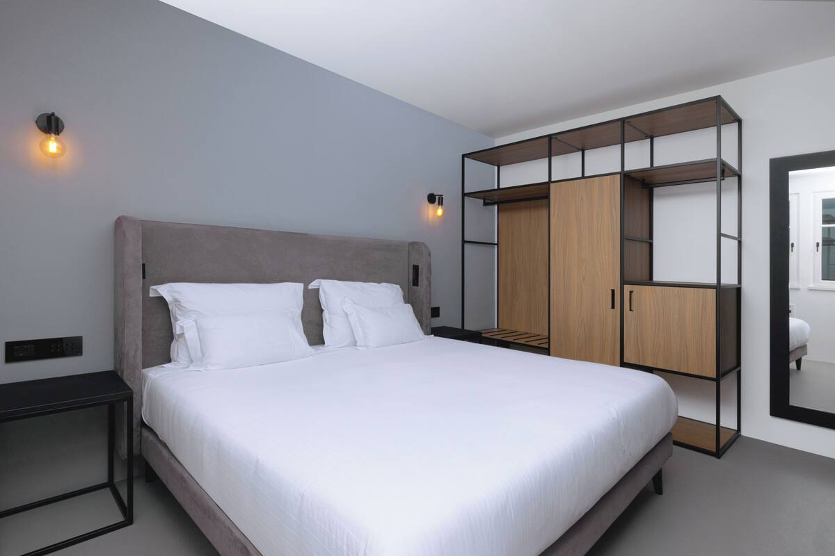 A modern bedroom with a large bed, a wooden wardrobe, and a nightstand.