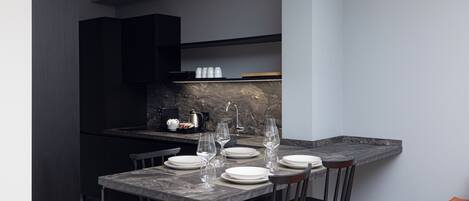 A modern kitchen with dark cabinetry, a marble countertop, and a dining area set for four with white plates and wine glasses.