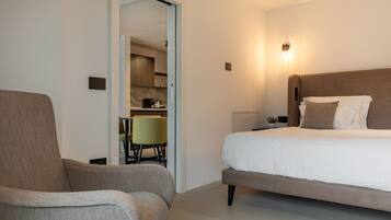 A modern hotel room with a large bed, a sofa, and a kitchenette in the background.