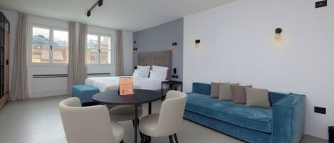Una habitación de hotel moderna con una cama, un sofá azul, una mesa de comedor con sillas y vistas a la ciudad.