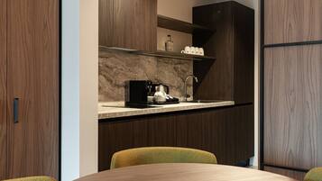 A modern kitchen with dark wood cabinets, a marble countertop, a coffee machine, and a sink. There are two chairs and a table in the foreground.