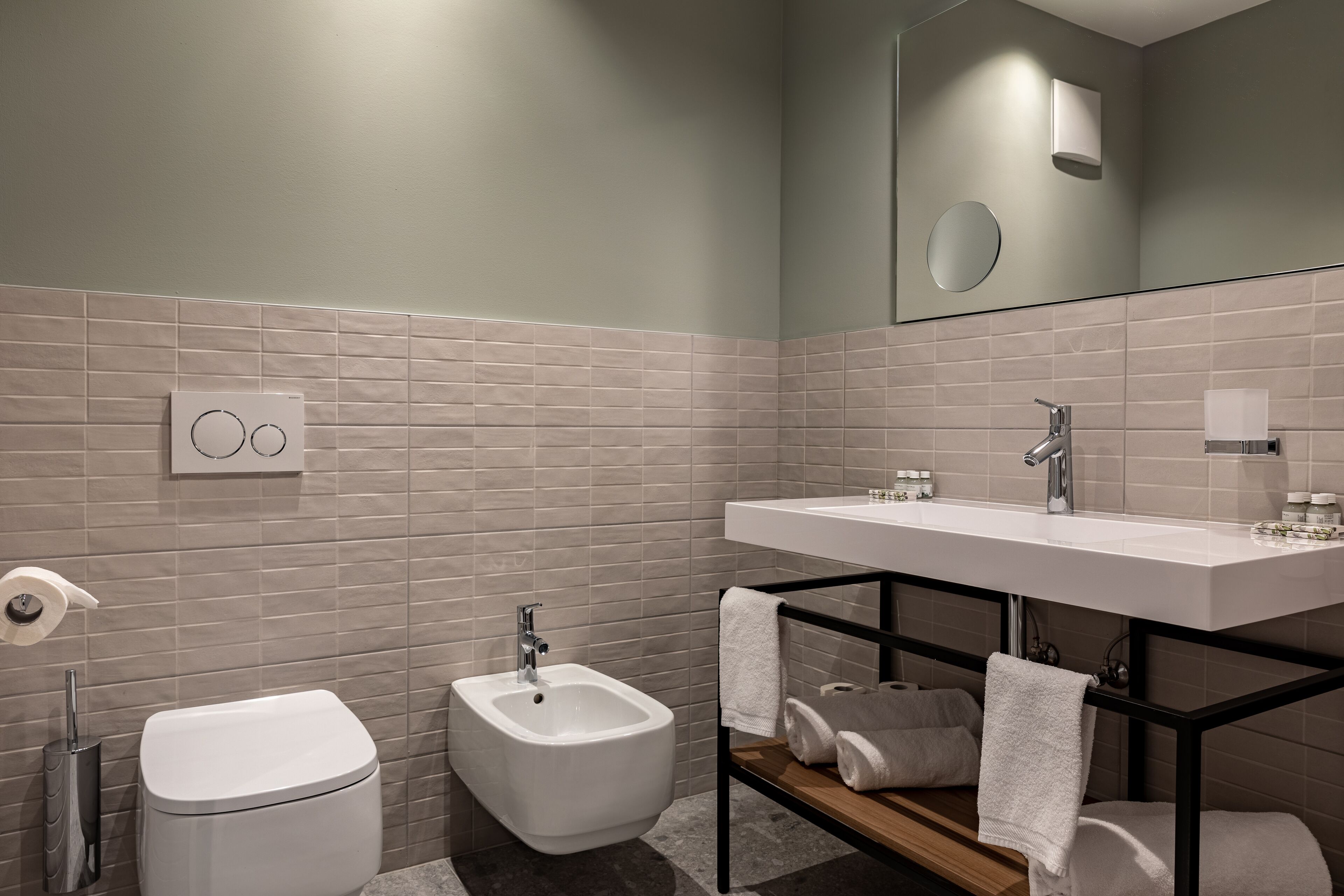 A modern bathroom with a bidet, toilet, and a large mirror above the sink.
