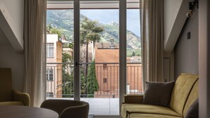 A room with a sofa, a table, and a view of a hillside with buildings. - Residence - Palais Hörtenberg (Bolzano)