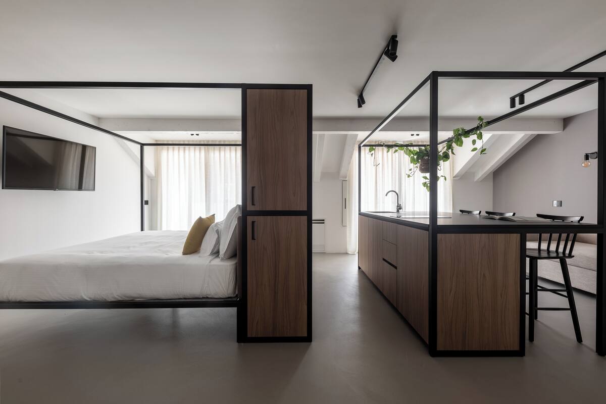 A modern, compact bedroom with a bed, a small desk, and a kitchenette.