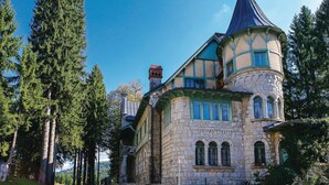 Ein historisches Steinhaus mit einem Türmchen, umgeben von hohen Bäumen.