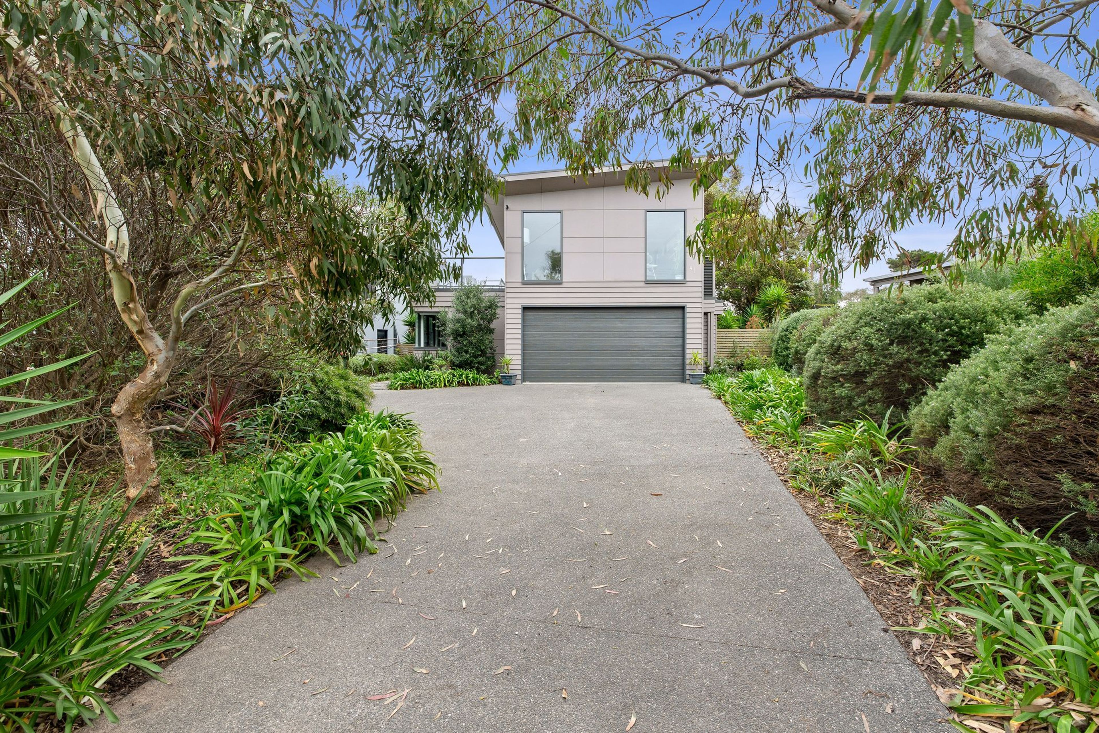 Une maison moderne à deux étages avec une allée pavée menant à un garage.