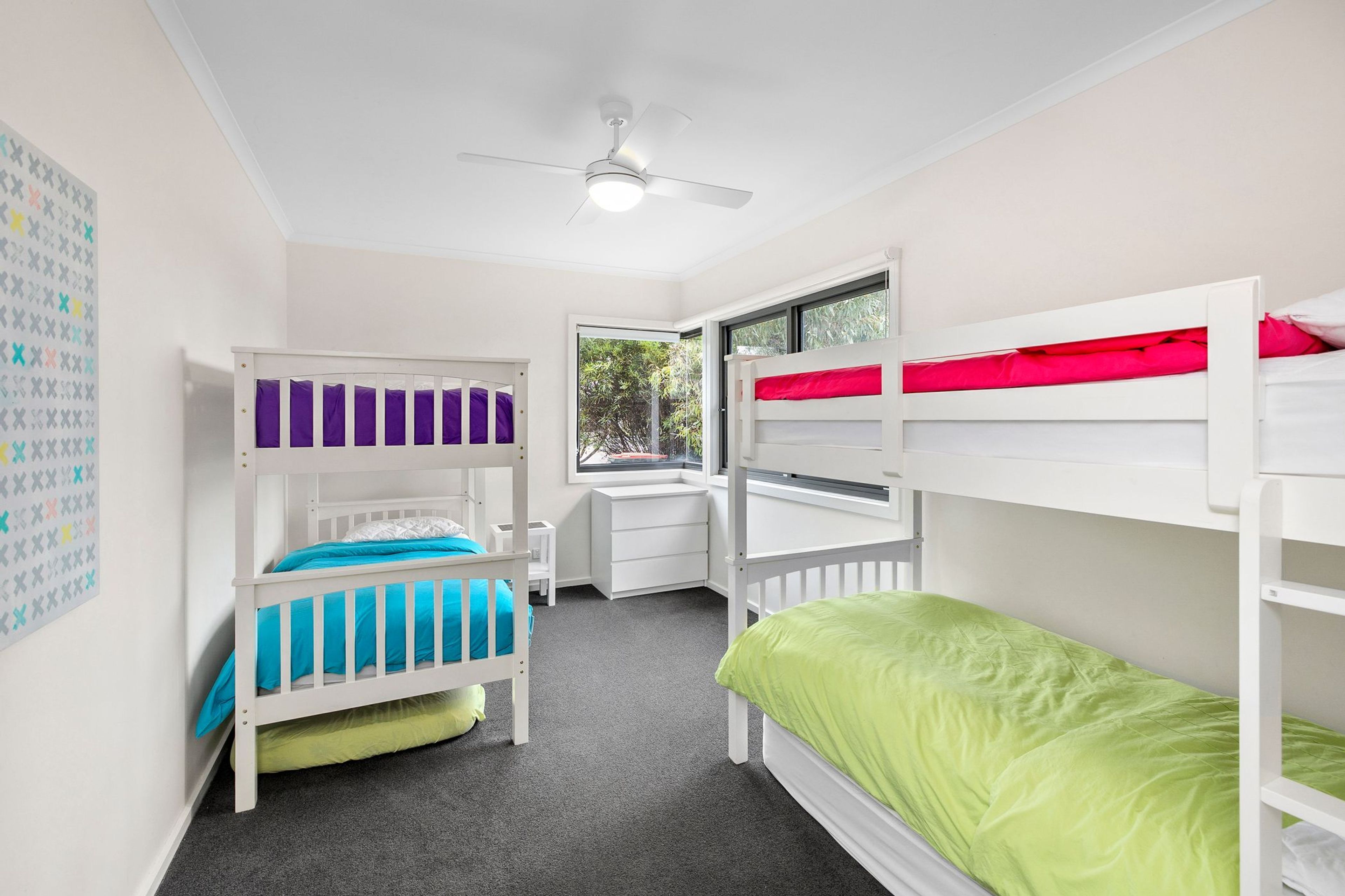 Une chambre d’enfant avec des lits superposés, un bureau et une fenêtre donnant sur un paysage verdoyant.