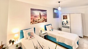 Een hotelkamer met twee bedden, een stadslandschap schilderij, een garderobe en bedlampen.