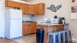 A kitchen with wooden cabinets, a white refrigerator, a microwave, and a sink. There are stools and a trash bin.