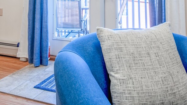 A room with a blue sofa, a white pillow, and a view of a balcony with a railing and a chair.