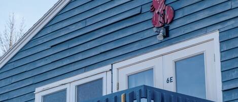 A blue building with a red rooster sign, a white door with the number 6E, and a blue railing.