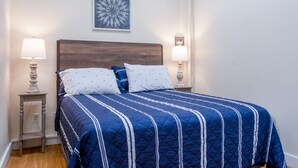 A neatly made bed with a blue quilt and white pillows, flanked by two bedside lamps on wooden nightstands.