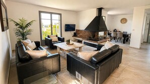 Een moderne woonkamer met een open haard, leren banken, een salontafel en een eethoek met stoelen.