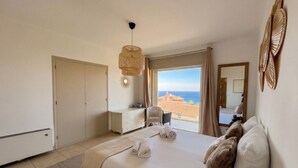 Een slaapkamer met een bed, een dressoir, een stoel, een groot raam met uitzicht, en een hanglamp.