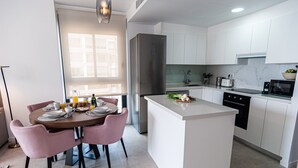 A modern kitchen with white cabinets, a stainless steel refrigerator, and a breakfast setup on the island. - A016 - ARENAL SUITES - AVANOA (Calpe)